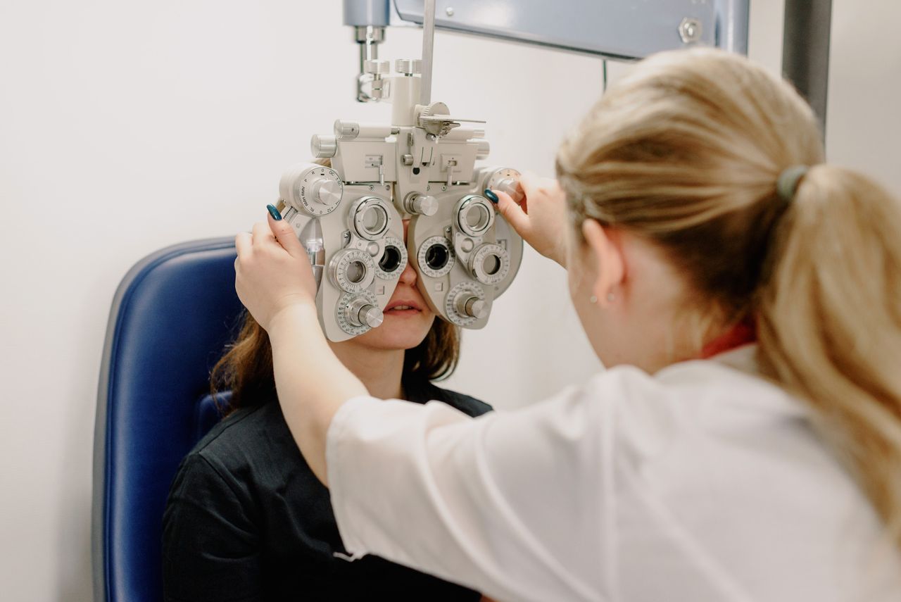 Anonymous female doctor in medical uniform doing eyesight measurement of patient with modern phoropter with lenses  in contemporary clinic