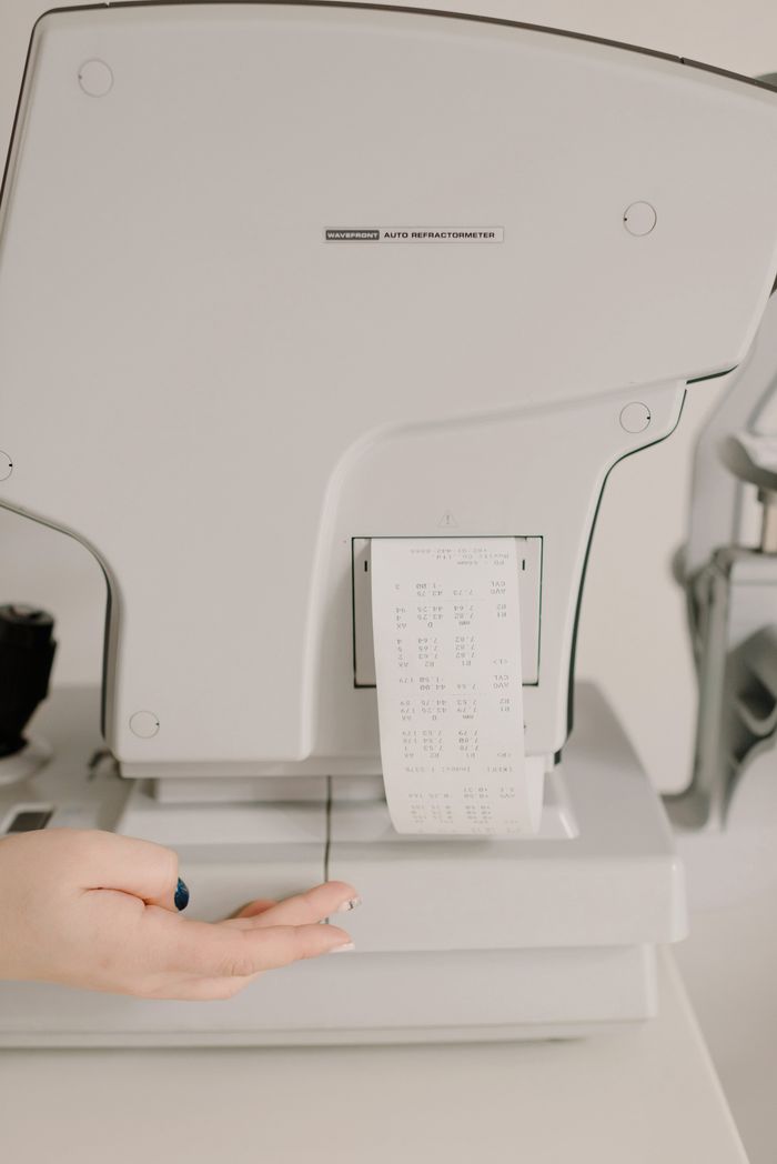 Crop anonymous oculist using professional vision screening device printing eye exam results on paper in clinic